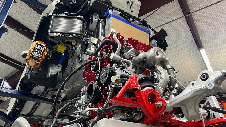 A custom built engine with a large turbocharger and performance brake caliper being installed in a workshop.