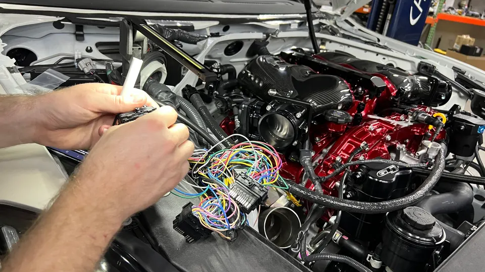 Mechanic working on the complex wiring harness of a high-performance Nissan GT-R engine during a custom build or tuning session.