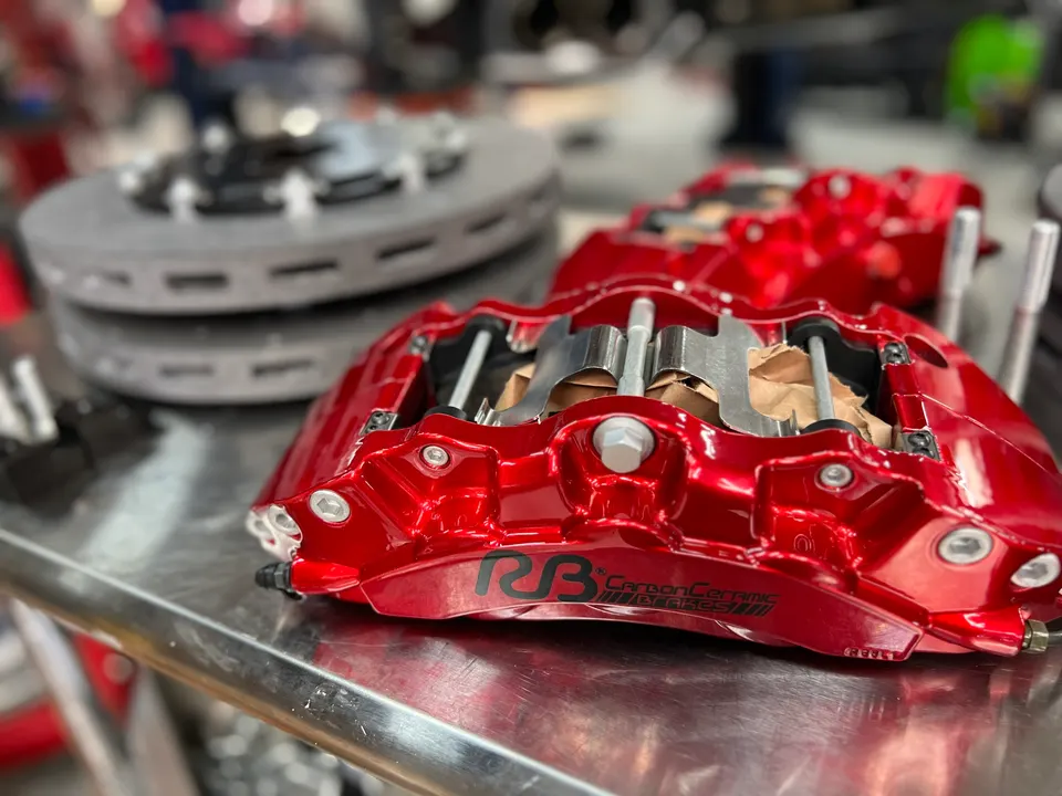 Red performance brake calipers and rotors on a workbench in a tuning shop, ready for installation.