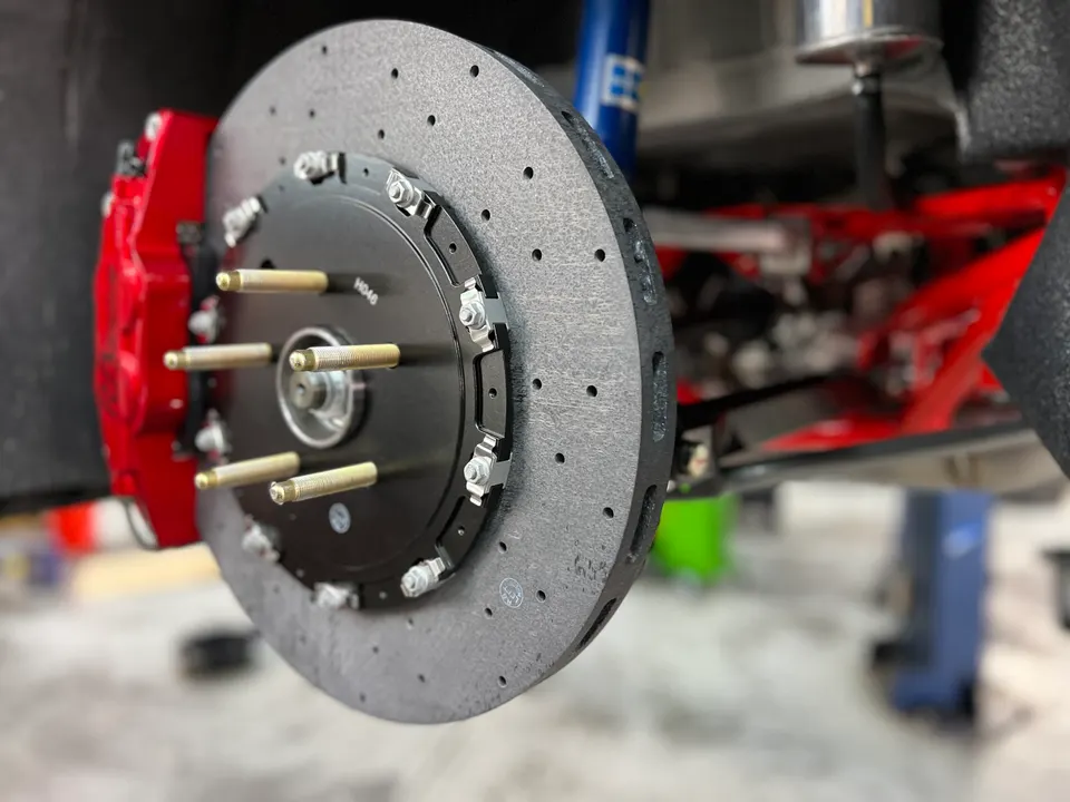 Close-up of a high-performance brake system with a large drilled rotor, red caliper, and wheel studs in a shop.