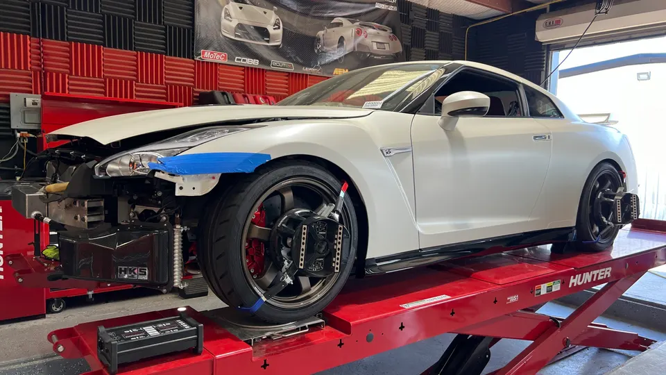 A white Nissan GT-R on a red Hunter alignment rack in a performance tuning shop, with the front bumper removed.