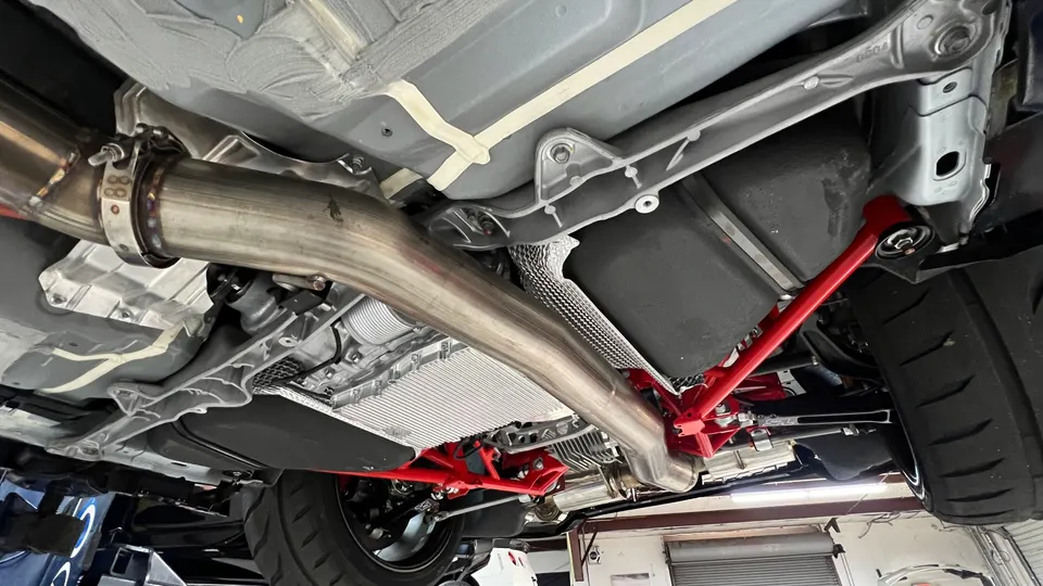 Underside view of a performance car showcasing an aftermarket stainless steel exhaust system and red chassis bracing.