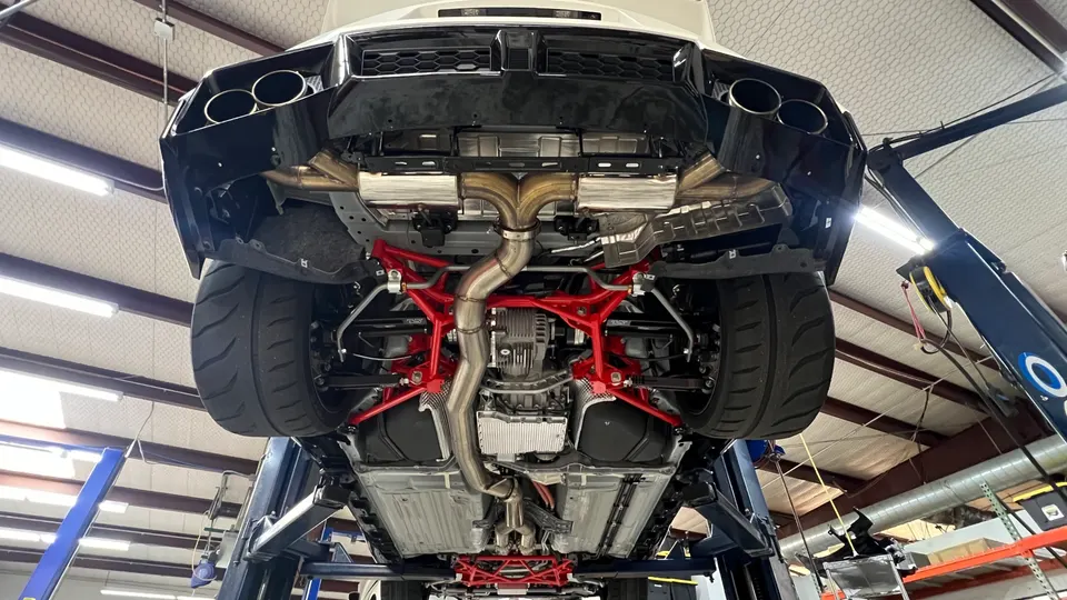 Underside view of a Nissan GT-R on a shop lift, showcasing an aftermarket exhaust system and red suspension components.