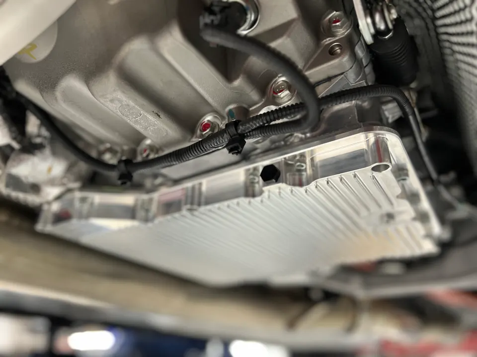 Close-up of an aftermarket finned transmission pan installed on a performance vehicle, likely for improved cooling.