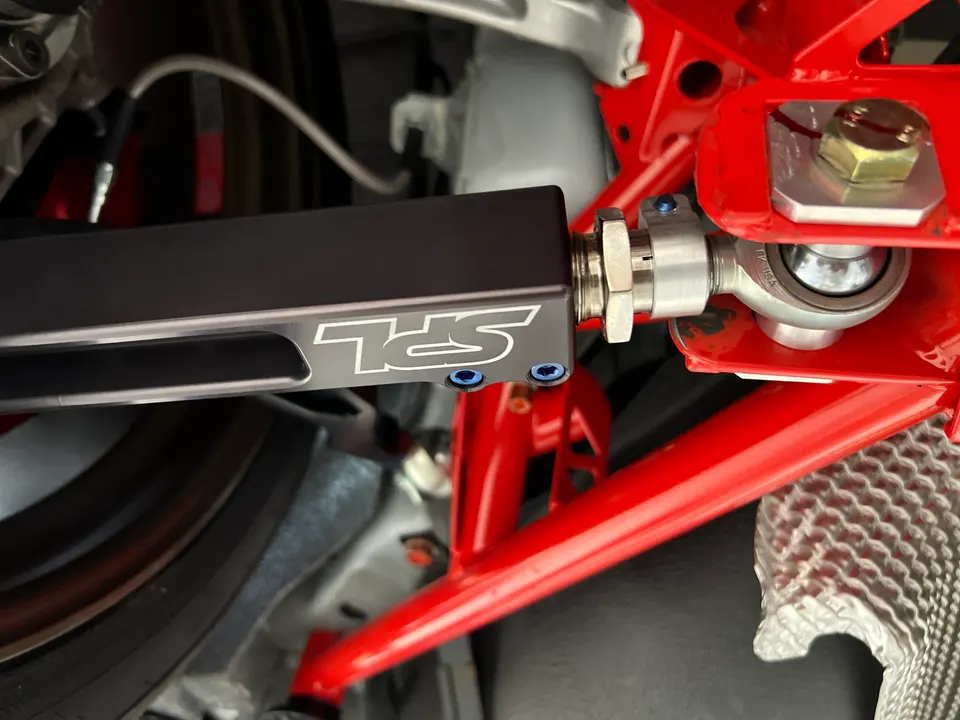 Close-up of an SPL adjustable control arm installed on a red chassis component of a performance car.