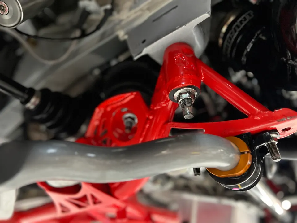 Close-up of a car's undercarriage showing red aftermarket suspension control arms and sway bar installation.