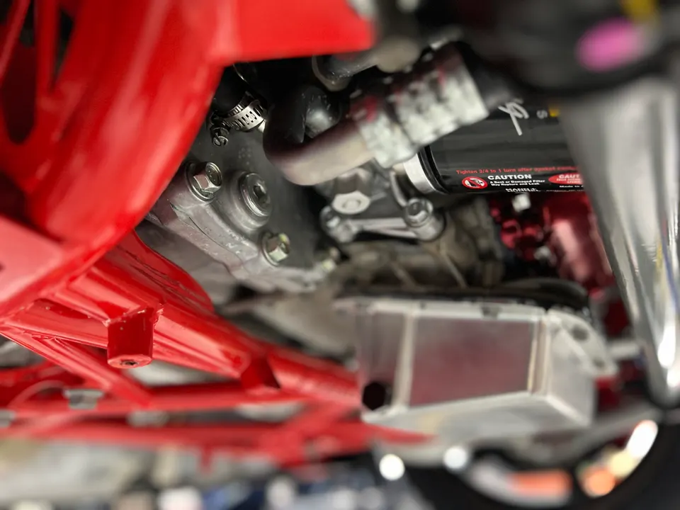 Close-up view of a performance car's underside, showing the custom red chassis, engine oil pan, and drivetrain components.
