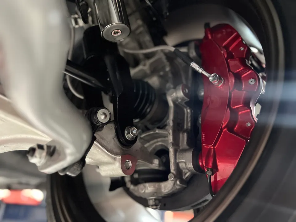 A close-up view of a car's red brake caliper, rotor, and suspension components.
