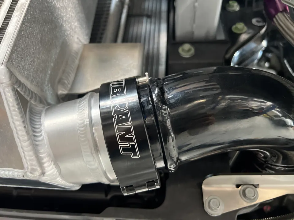 Close-up of an intercooler pipe connected with a Vibrant clamp, showcasing the aluminum welds in an engine bay.