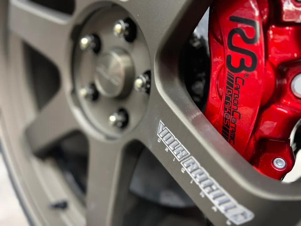 A close-up of a bronze Volk Racing wheel with a red Brembo Carbon Ceramic brake caliper.