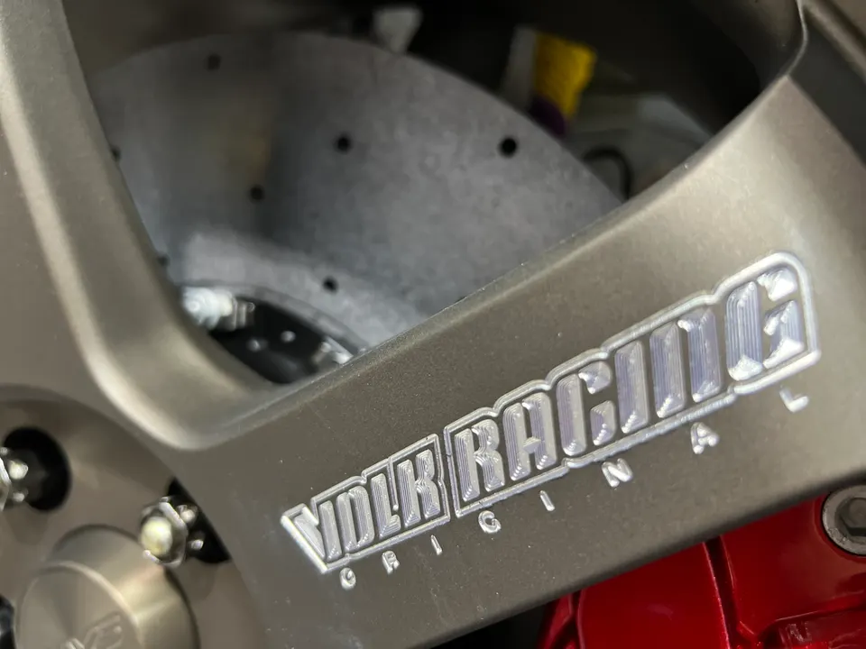 Close-up of a Volk Racing wheel with a red brake caliper and drilled rotor on a performance car.