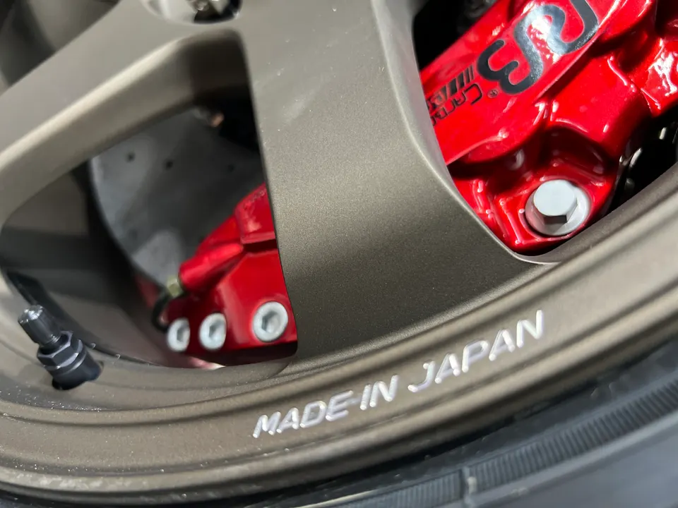 Close-up of a bronze multi-spoke wheel with a red brake caliper, featuring 'MADE IN JAPAN' text on the wheel rim.