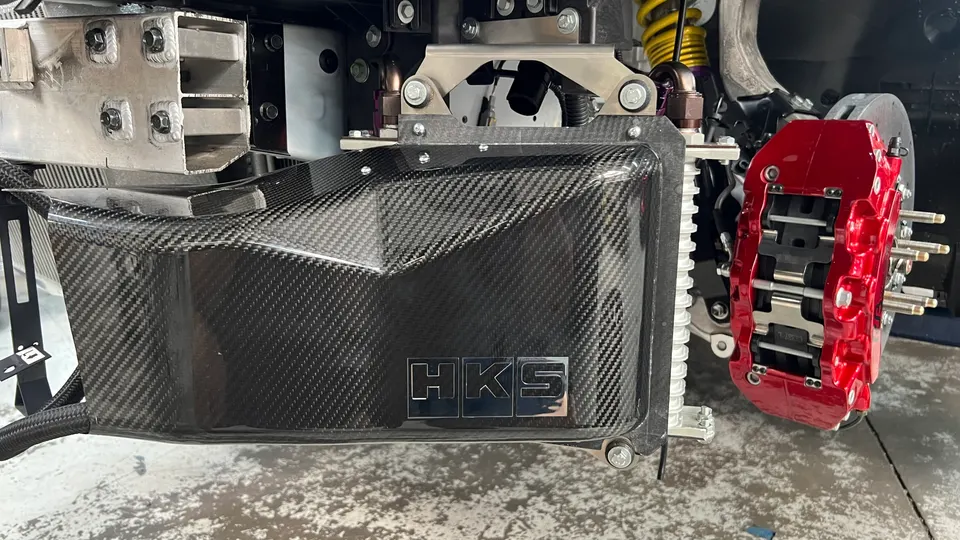 A close-up of a carbon fiber HKS intake system and a red brake caliper on a performance car.
