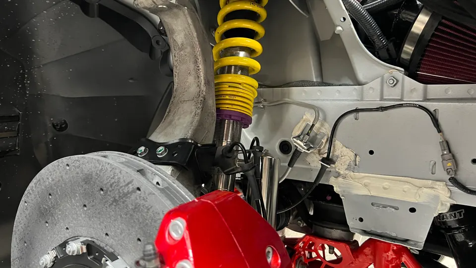 Close-up of a car's performance suspension with yellow coilovers, red brake calipers, and a perforated brake rotor.
