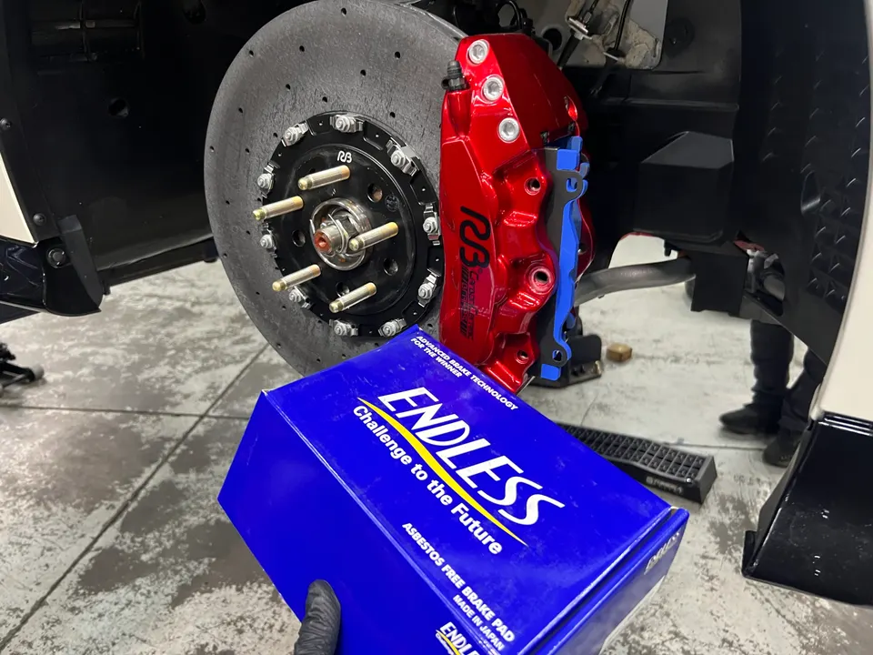 Close-up of a car's large red brake caliper and drilled rotor with a box of Endless brake pads in a shop.