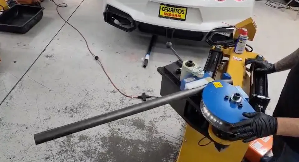 Mechanic bending a metal pipe for a custom car part on a Nissan GT-R in a performance shop.