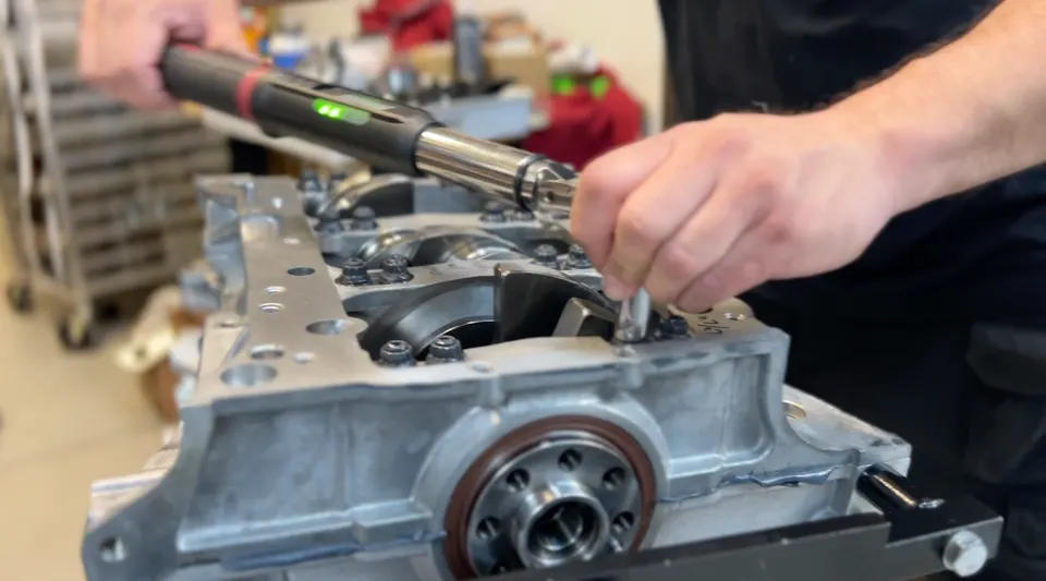 Mechanic using a torque wrench to assemble an engine block in a performance tuning shop.