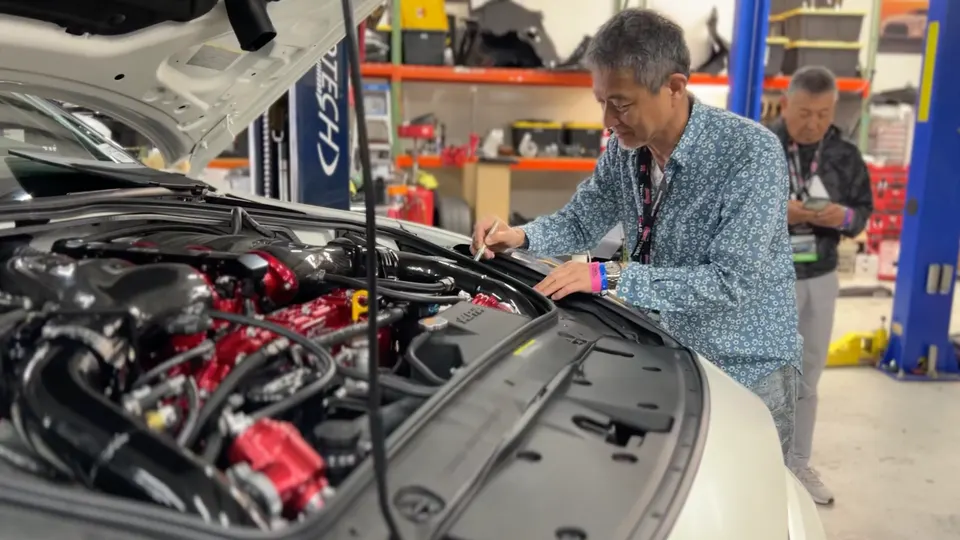 A mechanic inspects the modified engine bay of a performance car in a Jotech Motorsports shop.
