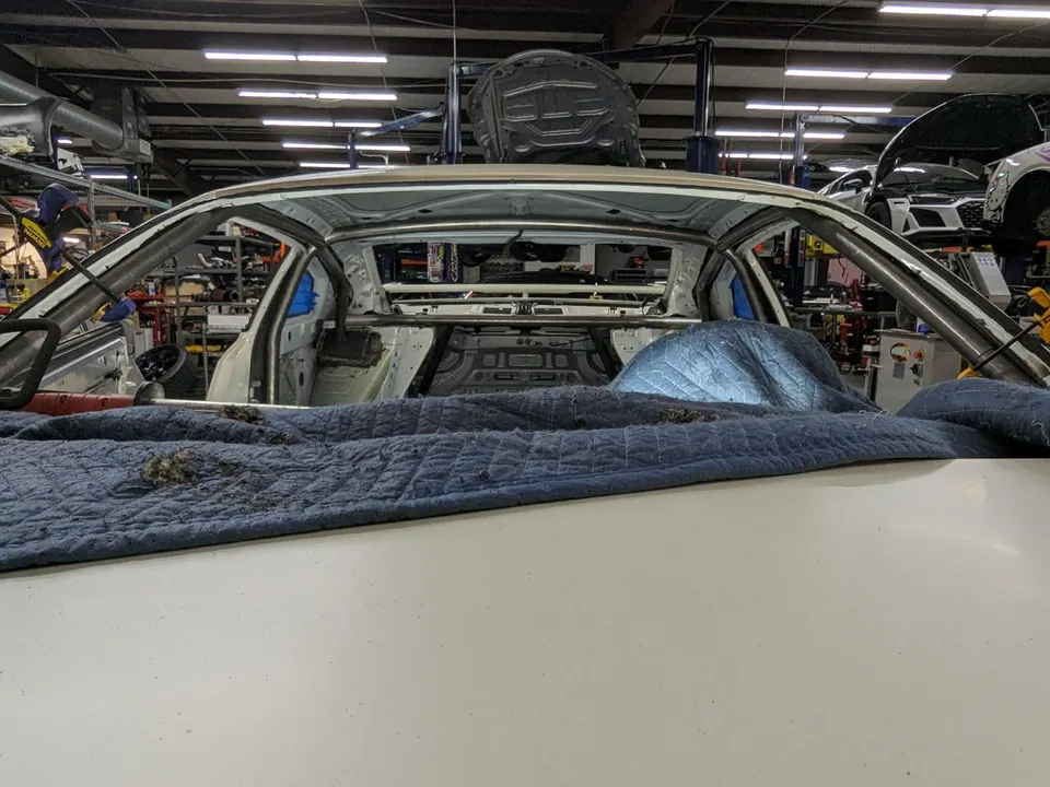 Roll cage installation in progress on a stripped car interior at a performance tuning shop.