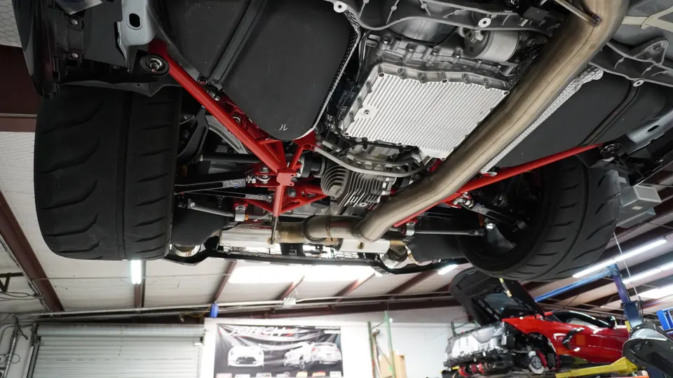 Underside view of a performance car on a lift, showcasing the exhaust system, differential, transmission, and wide tires.