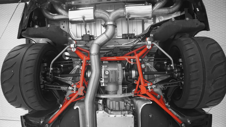 Underside view of a performance car showing custom exhaust, red chassis brace, differential, and wide rear tires.