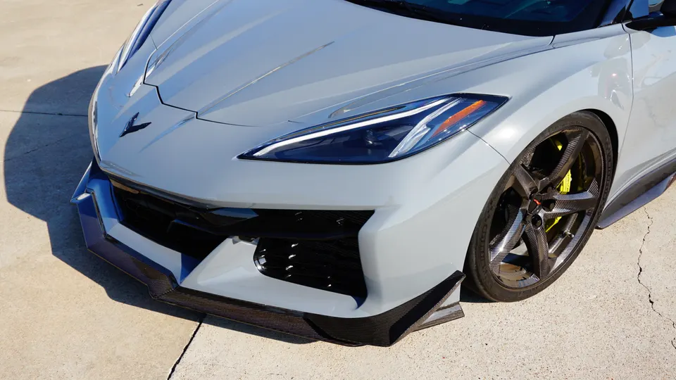 Close-up of a grey Chevrolet Corvette C8 front end, showcasing carbon fiber splitter, carbon wheels, and yellow brake calipers.