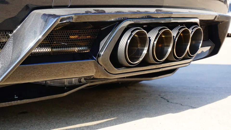A close-up of a car's rear bumper featuring quad carbon fiber exhaust tips and a black diffuser.