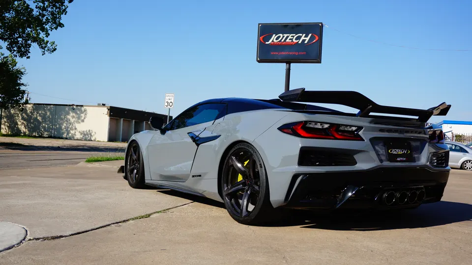 A grey Corvette C8 Z06 with a large rear wing and quad exhaust tips parked outside Jotech Racing.