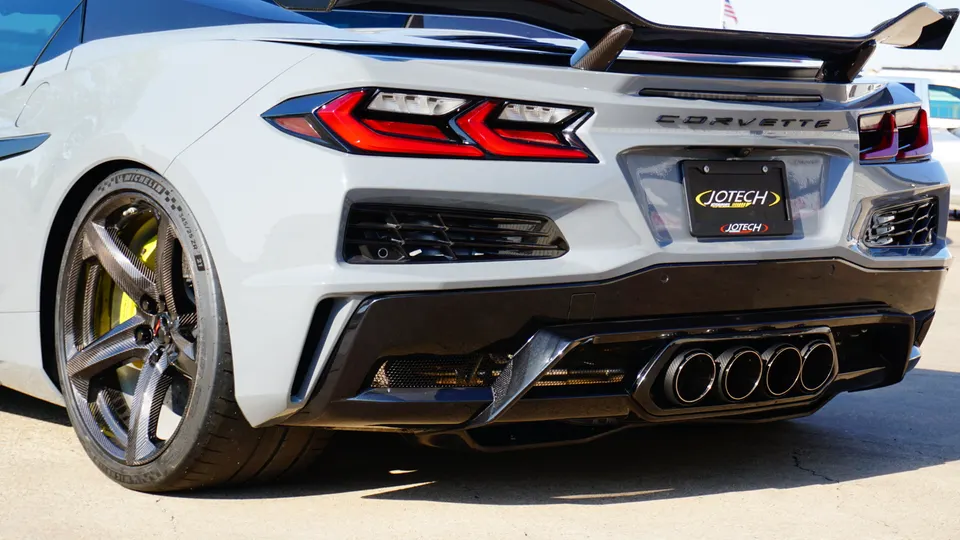 Rear view of a white Chevrolet Corvette C8 with custom carbon fiber wheels, quad exhaust, and a carbon fiber spoiler.