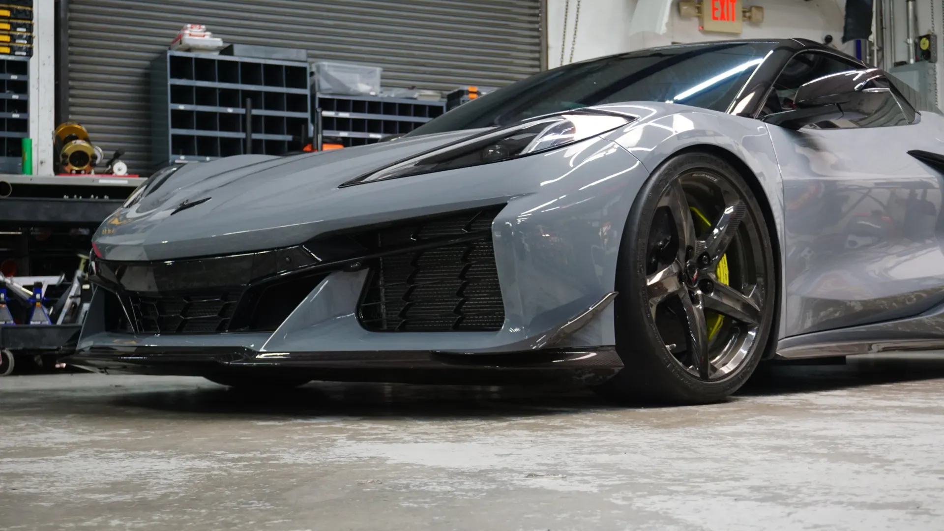 Grey Chevrolet Corvette C8 with carbon fiber front splitter and custom wheels with yellow brake calipers in a performance shop.