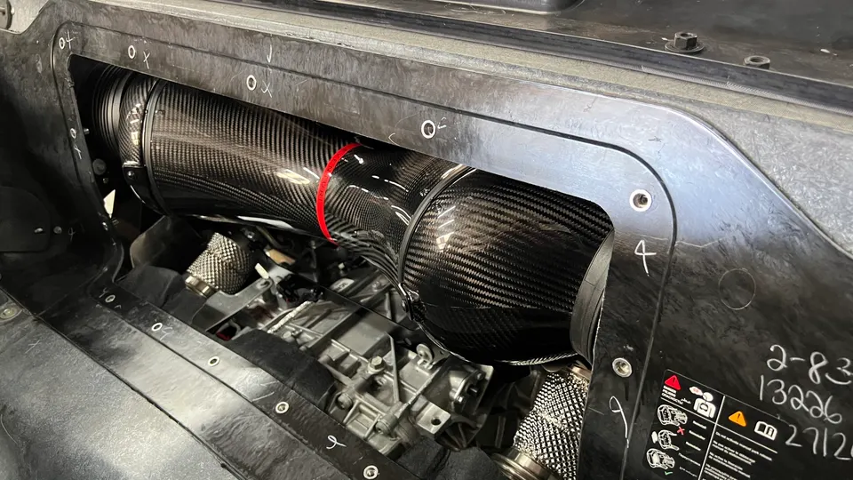 A close-up view of a carbon fiber intake system installed in the engine bay of a high-performance car.