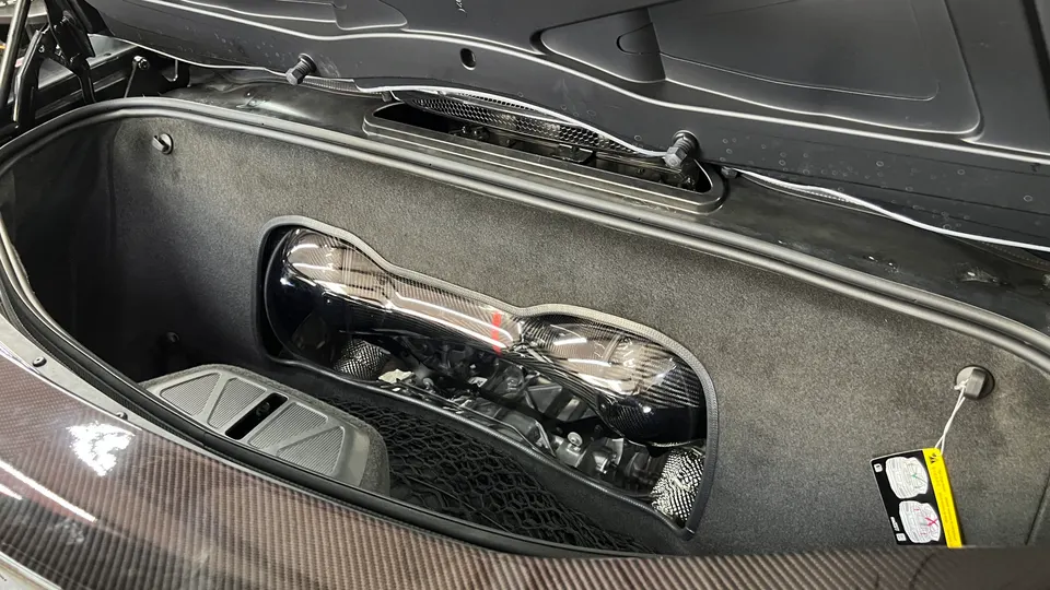 Close-up of a McLaren frunk with a carbon fiber engine cover and visible intake system components.