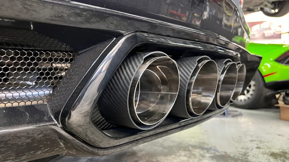 Close-up of a car's quad carbon fiber exhaust tips and rear bumper in a performance shop.