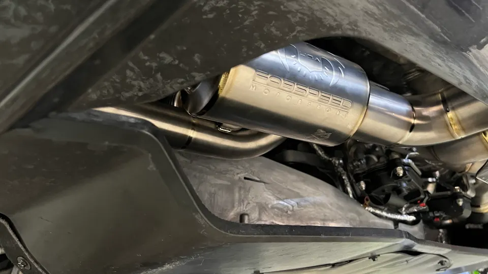 Close-up view of a Forspeed Motorsport stainless steel exhaust system installed on the underside of a performance car.