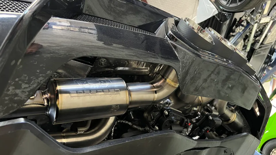 Close-up of a Porsche's aftermarket exhaust system with a polished muffler and custom piping installed in a shop.