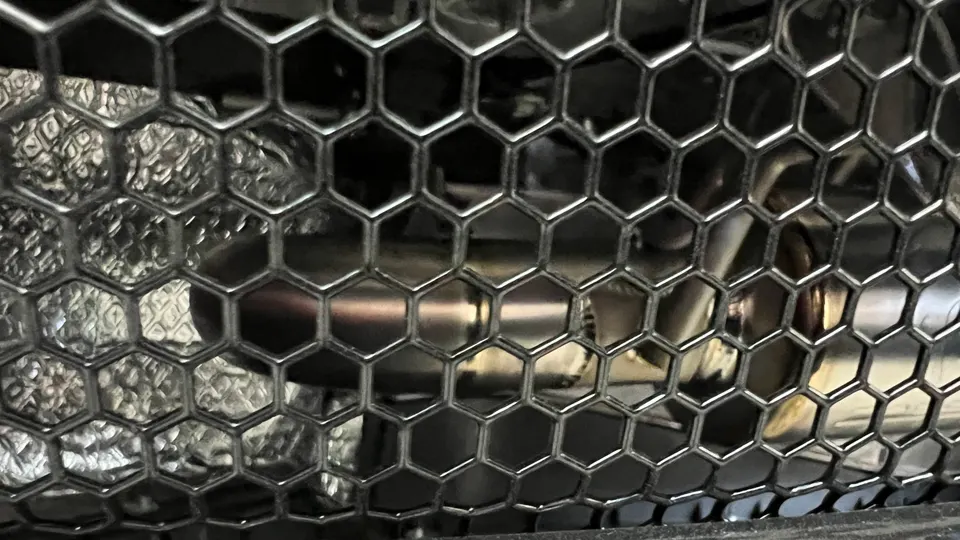 Close-up view of a performance exhaust system with a hexagonal grille and heat shielding.