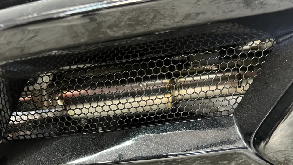 Close-up detail of a car's rear bumper with a honeycomb grille revealing a performance exhaust system.