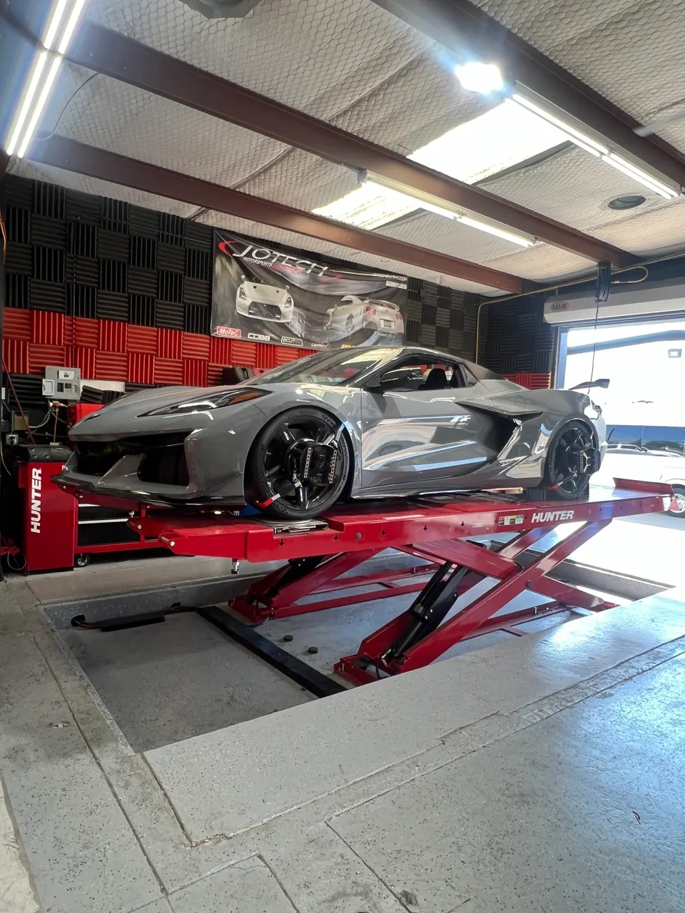 Grey C8 Corvette on a red hydraulic lift in the Jotech Motorsports tuning shop