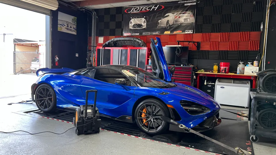 Blue McLaren 720S strapped to a dynamometer at Jotech Motorsports for performance tuning in a garage.