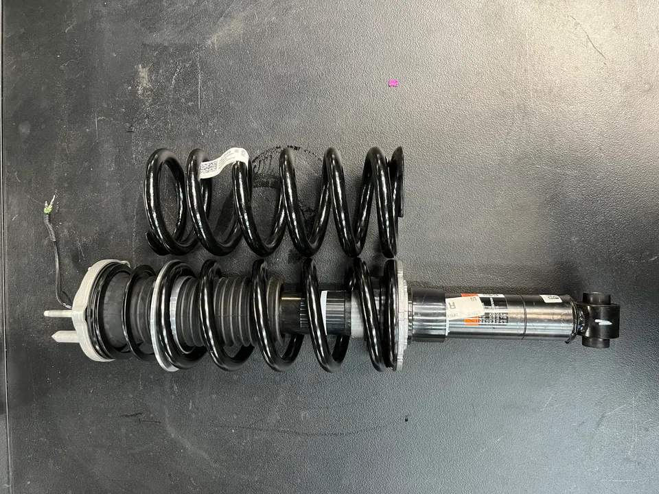 OEM shock absorber and spring for a car's suspension system, laid out on a dark shop surface.