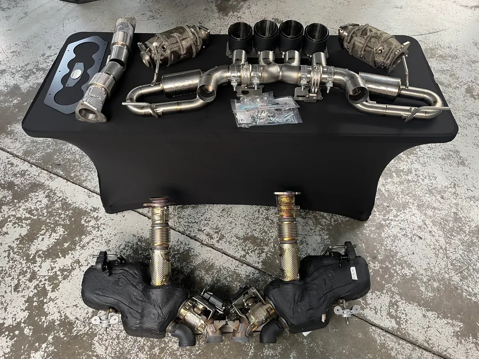 High-performance exhaust system components including downpipes, mufflers, and catalytic converters laid out in a shop.