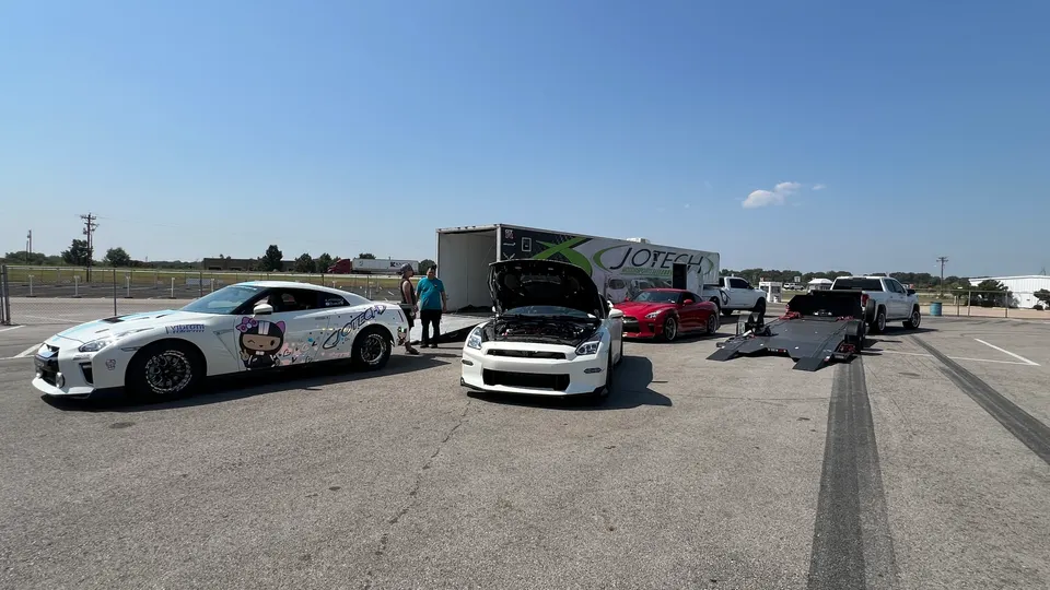 Two Nissan GT-Rs and a red sports car at a track day event with a Jotech Motorsports trailer and a car hauler.