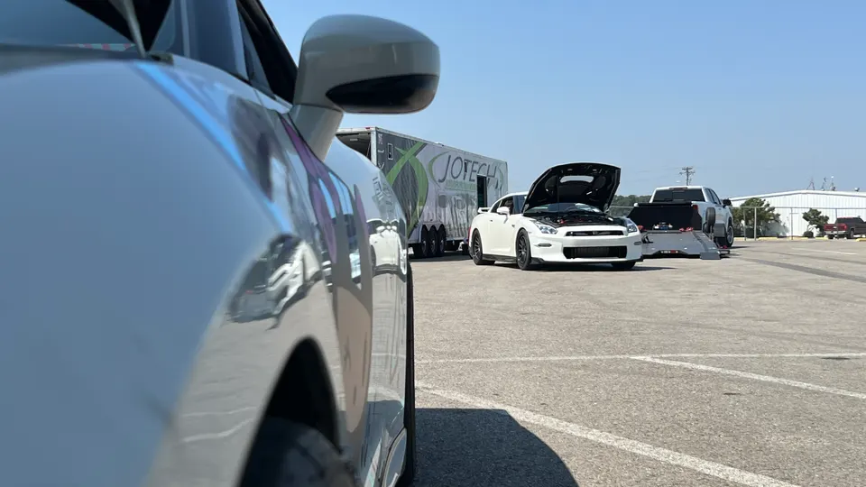 A white Nissan GT-R with its hood open, parked at a track event next to a Jotech Motorsports trailer.