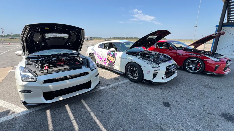 Three modified Nissan GT-R R35s with open hoods showcasing their engines, parked at a track on a sunny day.
