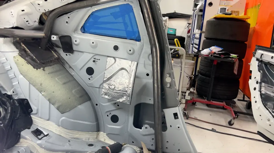 Interior view of a car undergoing a build in a shop, showing a roll cage being fabricated and installed.
