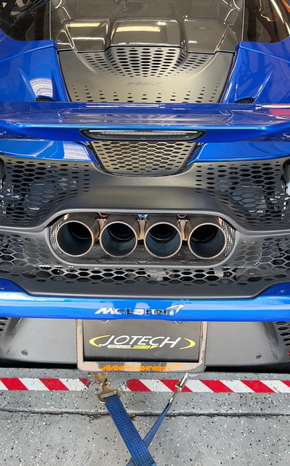 A blue McLaren 765LT on a dyno at Jotech Motorsports, showcasing its quad exhaust tips.