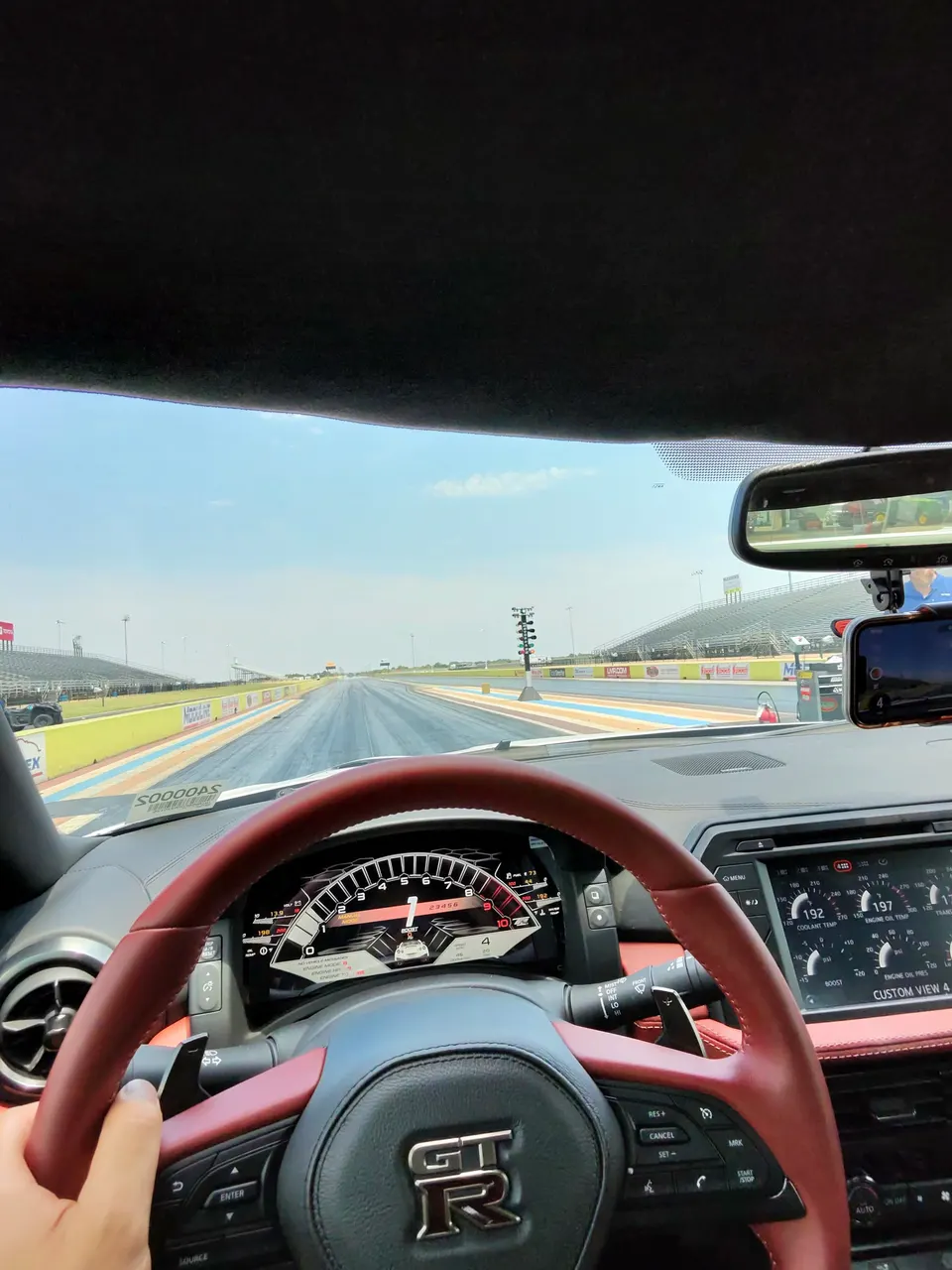 Driver's view from a Nissan GT-R on a drag strip, showing the dashboard, steering wheel, and track ahead.