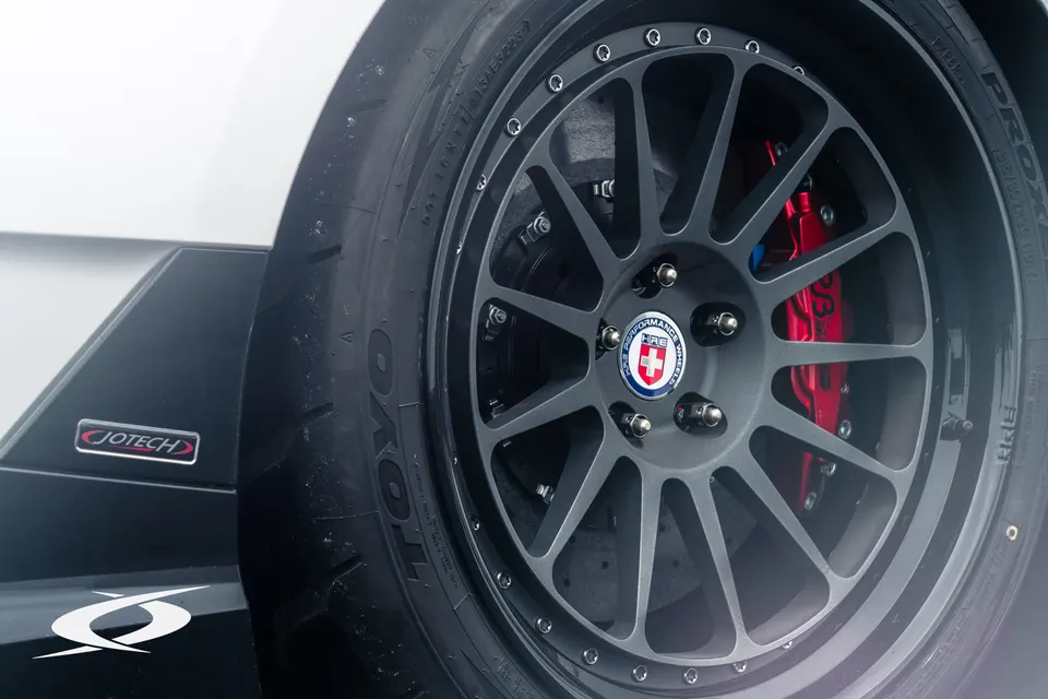 Close-up of a car's HRE performance wheel, Toyo tire, and red brake caliper, showcasing Jotech branding.