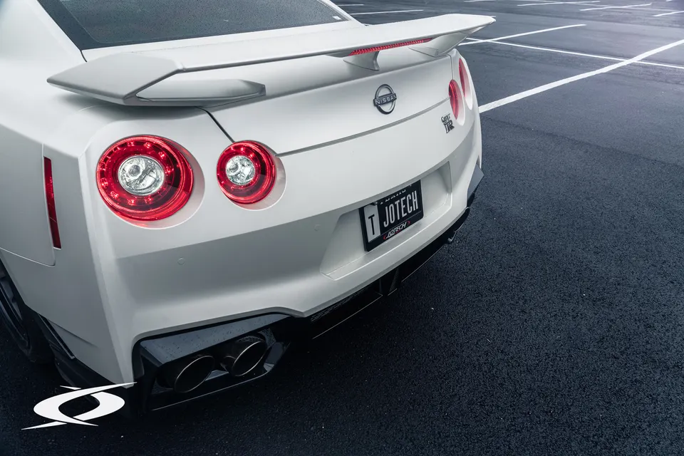A white Nissan GT-R from the rear, showcasing its spoiler, round taillights, and quad exhaust tips.