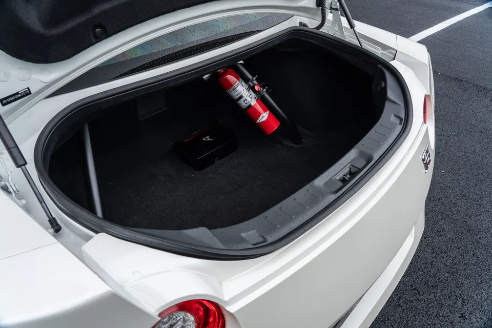 Open trunk of a white Nissan GT-R with a mounted fire extinguisher and black carpet.